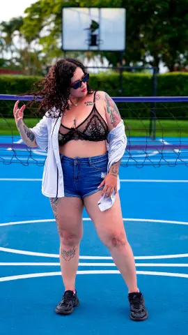 kayllaEvanss poses on a blue court wearing a black lace bra, denim shorts, and an open white shirt with sunglasses and tattoos visible.