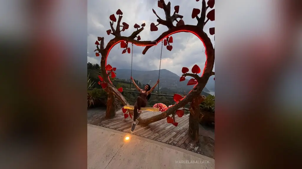 MarcelaBallack — Woman in a brown bikini relaxing on a heart-shaped swing overlooking a scenic mountain landscape at sunset.