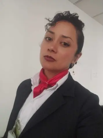 Professional woman in a black blazer and red scarf posing in an office setting with a confident mood.