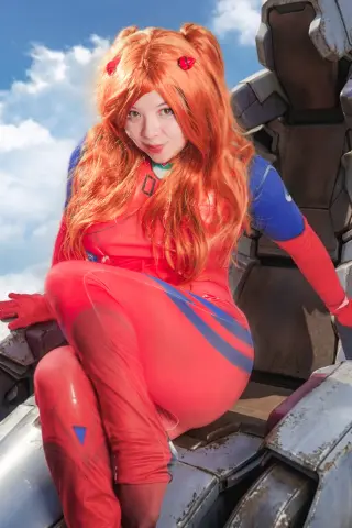 Cosplayer in a red Starfire superhero outfit sitting on a mechanical prop against a blue sky background.