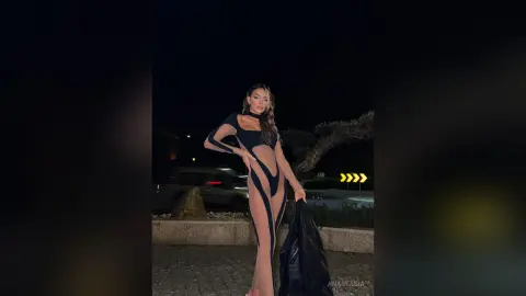 Anastasia poses outdoors at night wearing a black cut-out bodysuit that exposes her stomach and hips.