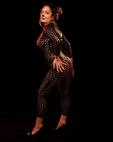 Woman in a black cutout bodysuit posing confidently against a dark background.