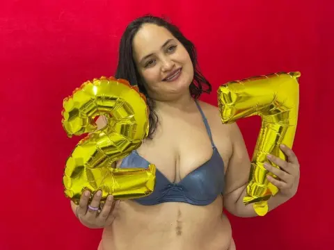Smiling woman in a blue bikini holding gold number 27 balloons against a red background for a birthday celebration.
