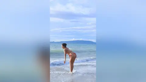 Fit woman in a red bikini playing in ocean waves under a bright blue sky at a serene summer beach.