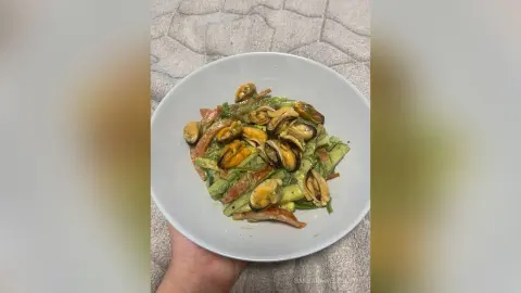 Fresh seafood pasta dish with mussels and zucchini served in a white bowl on a textured grey background.