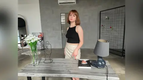 Young woman in a black halter top and beige trousers standing in a modern minimalist living room.