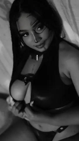 Young woman in a black halter top relaxing on white bedding in a moody black and white portrait.