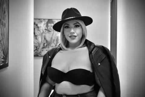 Stylish woman in a black hat and leather jacket posing confidently in a modern indoor setting.