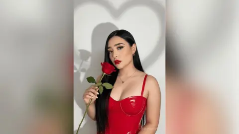 Glamorous woman in a red satin dress holding a single red rose against a soft heart-shaped shadow background.