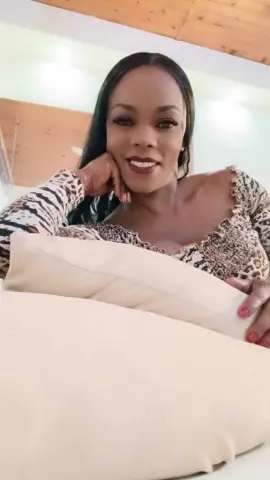 Smiling woman in a leopard print top relaxing on white pillows in a bright bedroom.