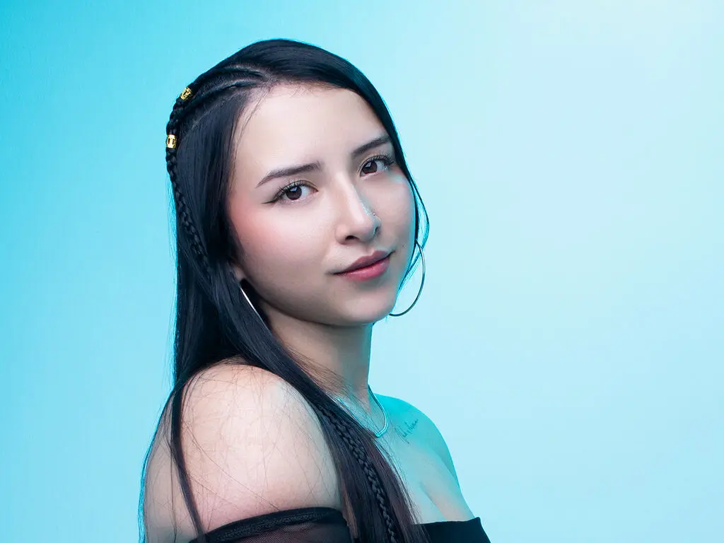 Fair-skinned woman in black tights sitting against a purple background in a moody, minimalist setting.
