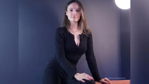 Elegant woman in a black long-sleeve top and dark jeans posing against a moody blue studio background.