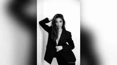 Elegant woman in a black blazer posing against a white wall in a moody black and white portrait.