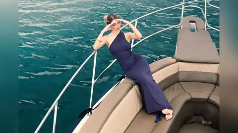 Elegant woman in a navy blue maxi dress relaxing on a luxury yacht in turquoise ocean waters.