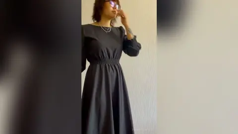 PenneySteinfeldt stands against a light wall wearing a long-sleeved black dress and silver necklace.