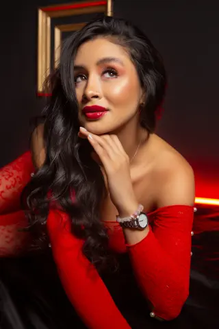 Beautiful woman in a red lace dress looking upward with a dreamy expression against a dark background.