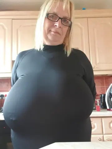 Blonde woman in a black long-sleeve turtleneck top standing in a bright kitchen setting.