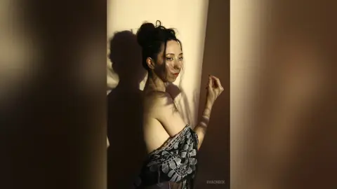Elegant woman in a black lace dress posing in dramatic shadows against a neutral wall.