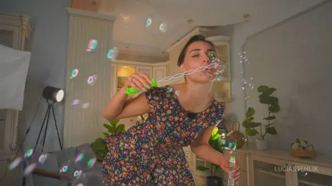Young woman in a floral summer dress blowing bubbles in a bright, whimsical indoor setting.
