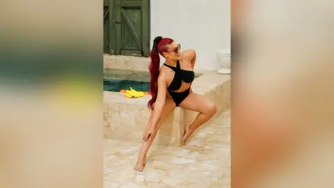 IsabellaEstrada poses in a black cut-out swimsuit by a stone pool, showing off her long red hair and tanned skin.
