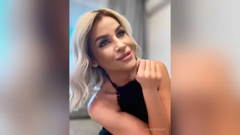 Blonde woman in a black halter top posing with a soft smile in a bright indoor setting.
