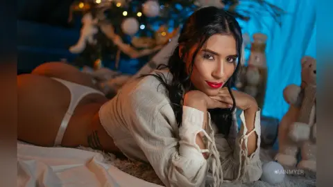 Beautiful woman in white loungewear relaxing on a bed near a festive Christmas tree in a cozy mood.