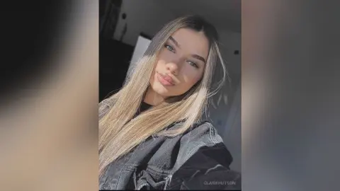 Young woman with long blonde hair wearing a black denim jacket in soft natural sunlight.
