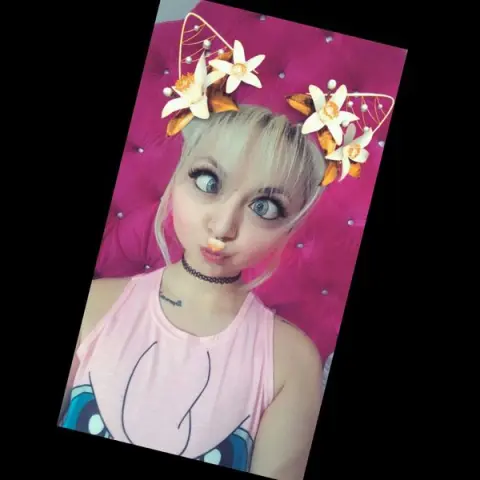 Blonde woman in a pink tank top wearing white flower cat ears against a bright pink background.