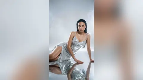 Elegant woman in a shimmering silver satin slip dress posing in a bright studio setting.