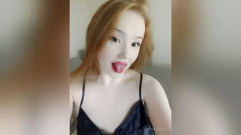 EpifaniaRalls sticks out her tongue while wearing a black camisole, showing her long light brown hair and face.