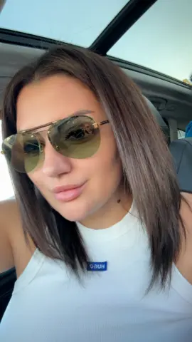 Stylish woman in white tank top and gold aviator sunglasses relaxing in a car with a sunroof.
