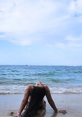 Relaxed woman in black bikini relaxing on a sunny beach by the turquoise ocean waves.