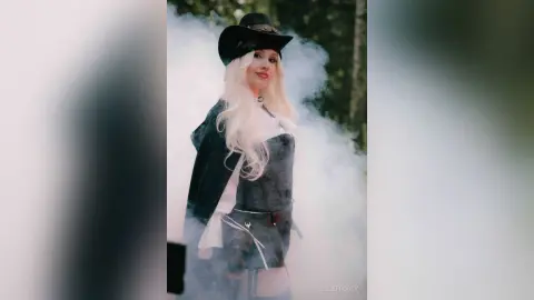 EllieFrosty wears a black cowboy hat and a dark denim-style top while standing in a light cloud of white smoke.