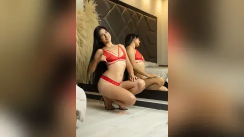 LauraMarcuzzi poses in red lace lingerie, wearing a red bra and red panties while kneeling on a bed in a room with a dark headboard.