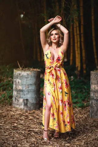 Blonde woman in a yellow floral maxi dress posing in a lush bamboo forest setting.