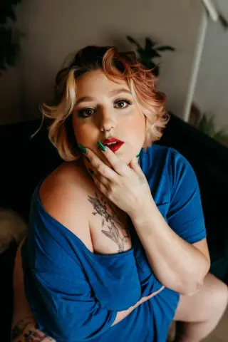Portrait of a blonde woman in a blue top posing thoughtfully in a cozy indoor setting.