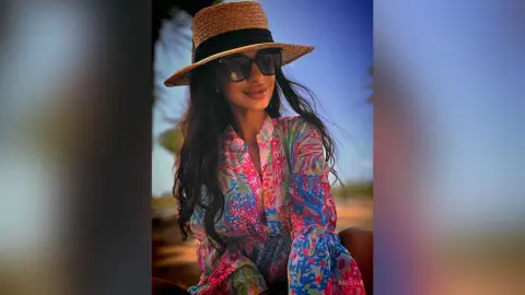 Smiling woman in colorful floral blouse and straw sun hat enjoying a sunny tropical vacation.