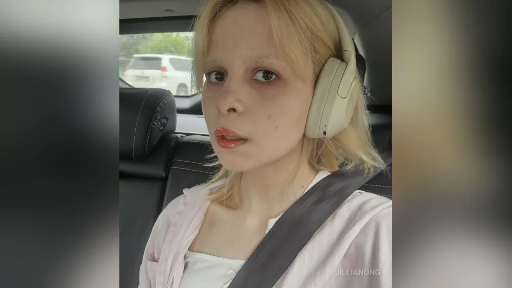 JillianOng — JillianOng wears white headphones and a white top while sitting in the back of a car.