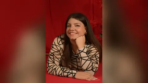 Smiling young woman in a black and beige geometric patterned top against a vibrant red background.