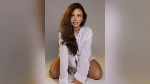 Elegant woman in a white button-down shirt posing with a confident smile in a minimalist studio setting.