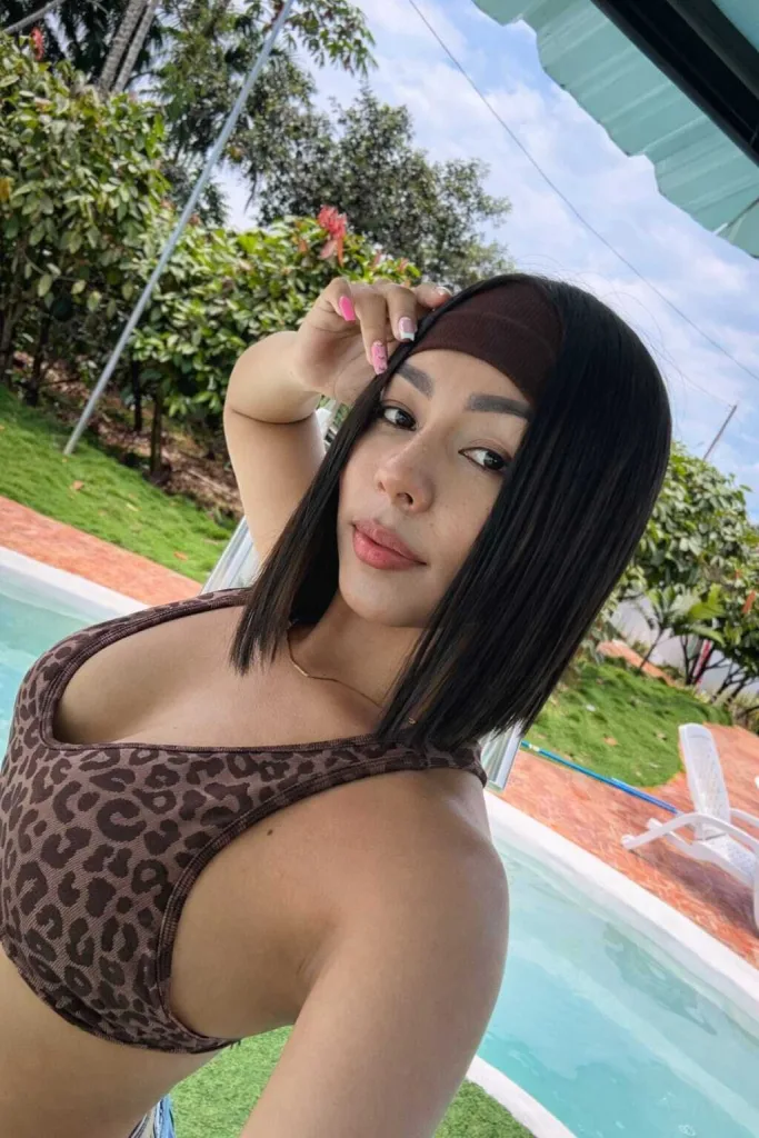 ZoeBrunet poses with her black hair styled in a bob with a pink headband, showing her bare shoulders and chest in a close-up shot.