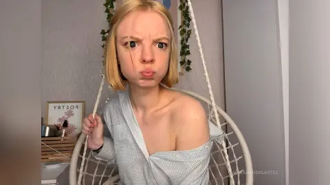 Blonde woman in a light blue checkered shirt making a funny face while sitting in a white hanging swing chair.
