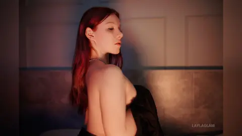 Redheaded woman in a black silk garment posing in soft, moody indoor lighting.