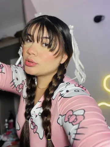Young woman with dark braids wearing a pink Hello Kitty pajama top in a cozy indoor setting.