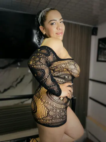 Woman in a black lace bodysuit posing in a modern living room with a confident mood.