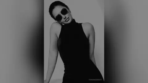 Stylish woman in a black sleeveless turtleneck and sunglasses posing against a minimalist studio background.