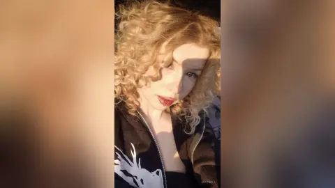 Blonde woman with curly hair wearing a black graphic hoodie in warm, cinematic sunlight.