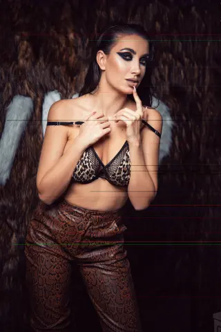 Glamorous woman in leopard print lingerie and snakeskin pants posing against a dark faux fur background.