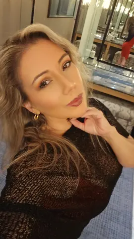 Blonde woman in a black textured sweater posing with a soft smile in a modern interior setting.