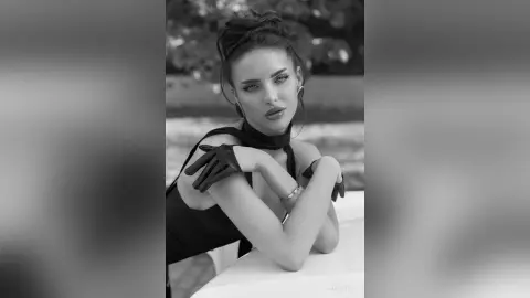 AnjeNoir poses in a black top and gloves, looking into the camera with her hair in a bun.
